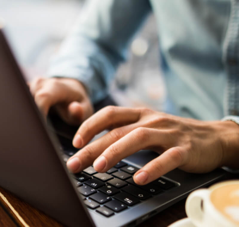 Un jeune homme tape quelque chose sur un ordinateur portable PEAQ, tasse de café à côté, assis dans un café, gros plan